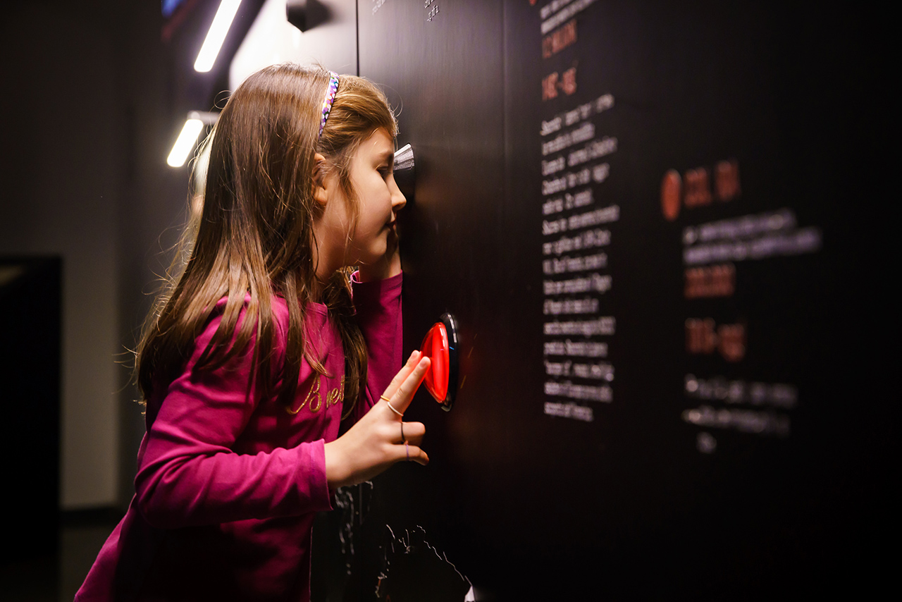 bambina di profilo che osserva dentro un oculare all’interno della sala della patologia al MUSME