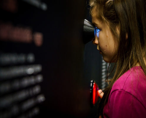 Bambina osserva all'interno di un oculare in una postazione interattiva nella sala della patologia del MUSME